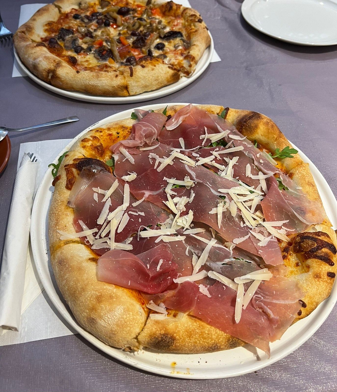 Prosciutto pizza with arugula and shaved cheese, a vegetable pizza behind it